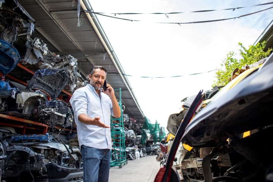 A man talks on a phone while standing among scrapped cars
